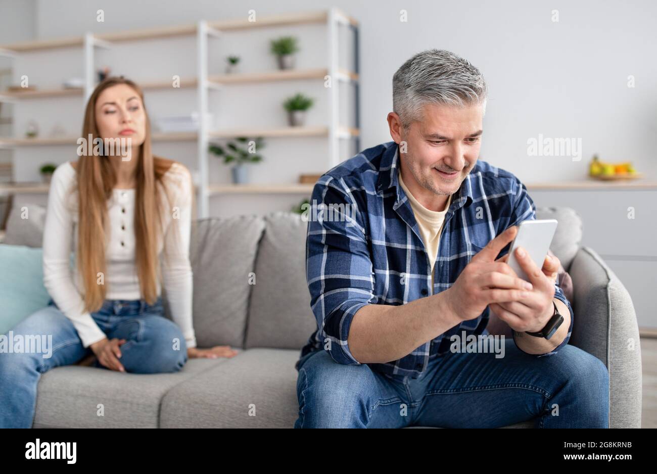 Ein älterer Mann vermeidet die Kommunikation mit seiner Frau, steckt in einem Mobilgerät fest, schreibt seinem Geliebten SMS, spielt Online-Spiele Stockfoto