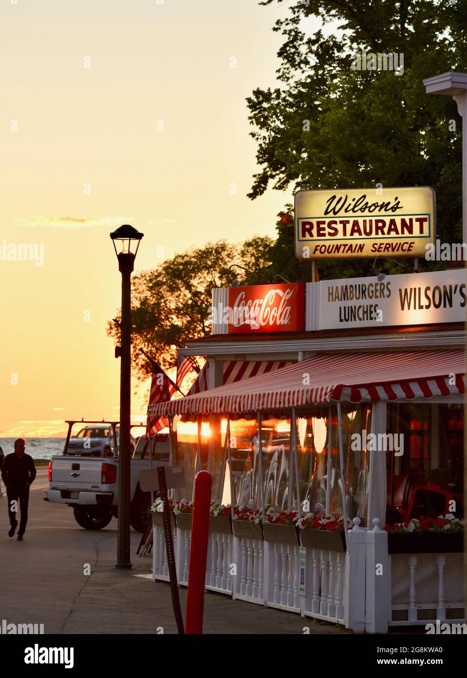 Herrlicher goldener Sonnenuntergang, der im Gelände reflektiert wird, mit Touristen, die zu Wilson's Ice Cream Parlor, gegründet 1906, Ephraim, Door County, Wisconsin, USA Stockfoto
