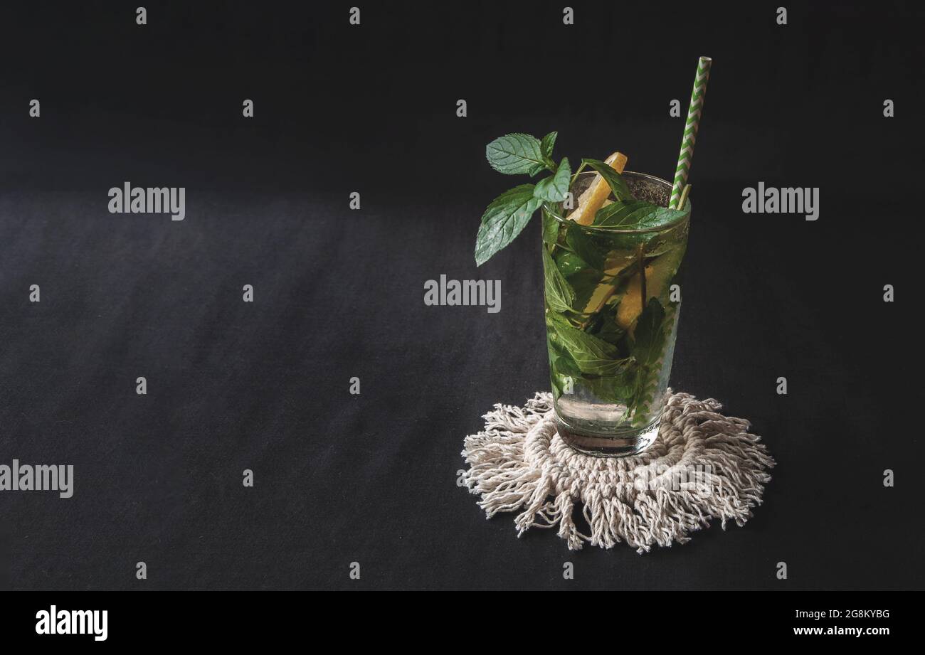 Sommerzitruscocktail Mojito mit Zitrone und Minze. Glas mit Pfefferminze mit Zitrusfrüchten auf schwarzem Hintergrund Stockfoto