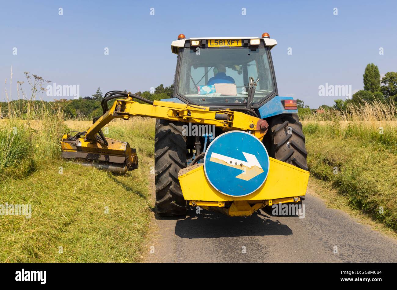 Mann in einem Traktor, der im Sommer Grasrändern auf einer Landstraße mäht. Much Hadham, Hertfordshire, Juli 2021 Stockfoto
