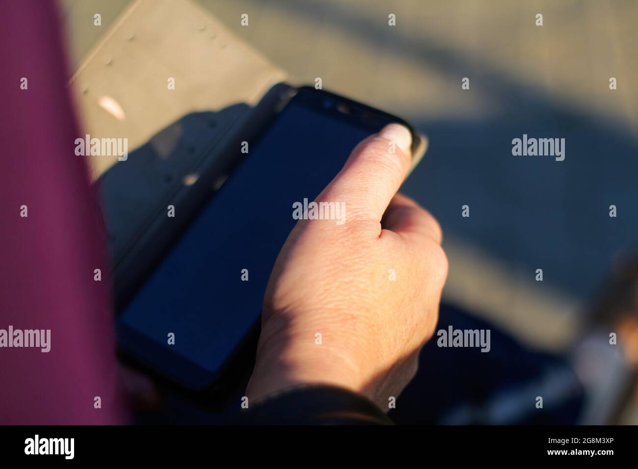 Unschärfe-Unschärfe-Nahaufnahme weibliche Hände suchen auf dem Telefon außerhalb, im Freien. Erwachsene Frau in lila Bluse mit Smartphone, während sie auf einer Bank in der p sitzen Stockfoto