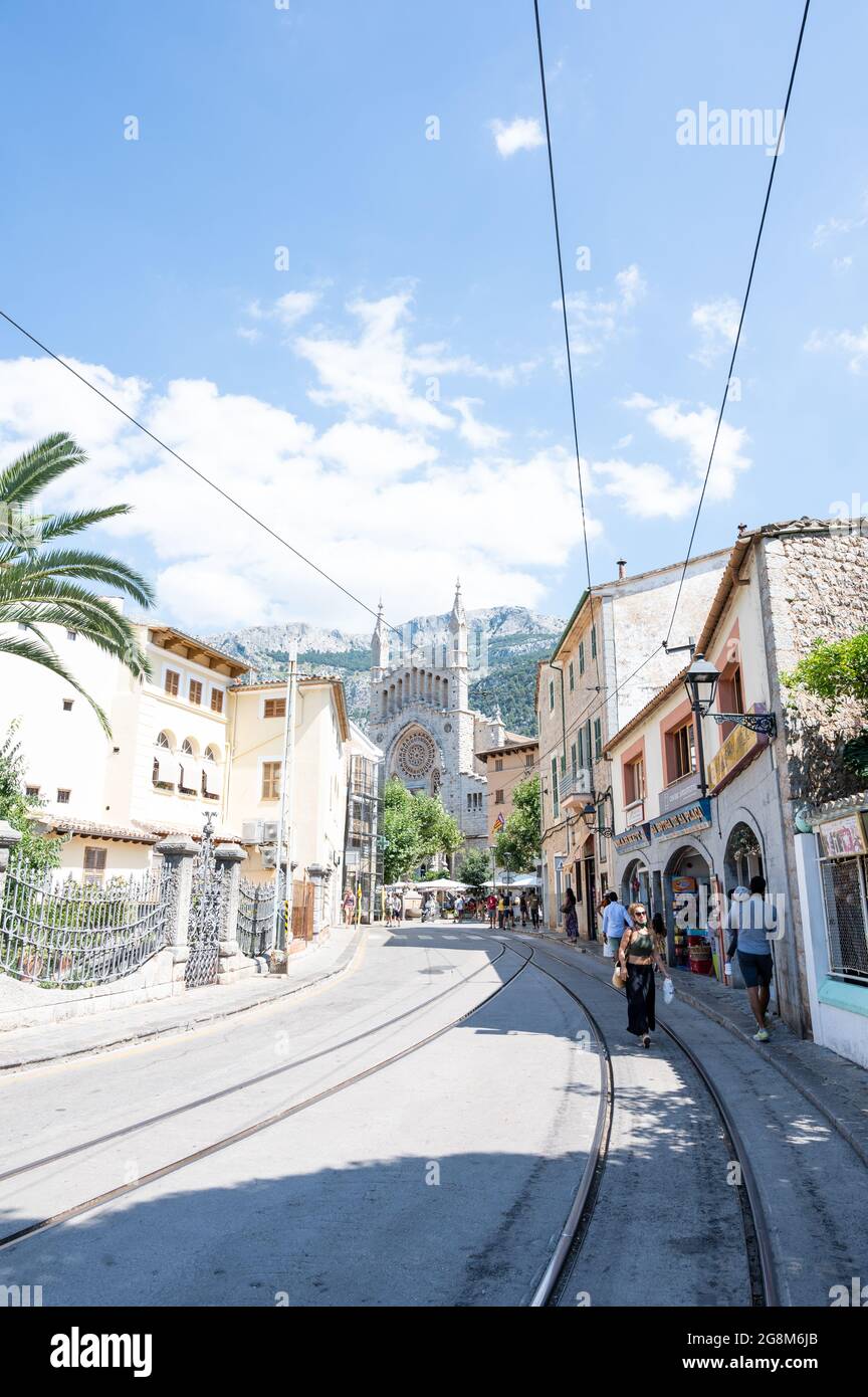 Soller, Spanien - 19. Juni 2021: Straße mit den Straßenbahnschienen und der Dorfkirche im Hintergrund Stockfoto