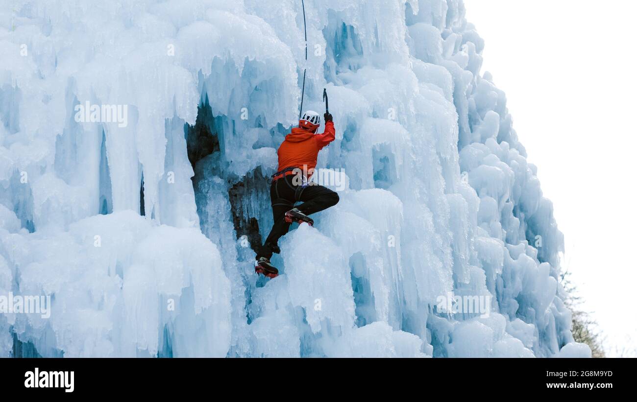 Mann klettert auf einem gefrorenen steilen Hang, vorbei zwischen großen Unebenheiten, Graten und Eiszapfen Stockfoto