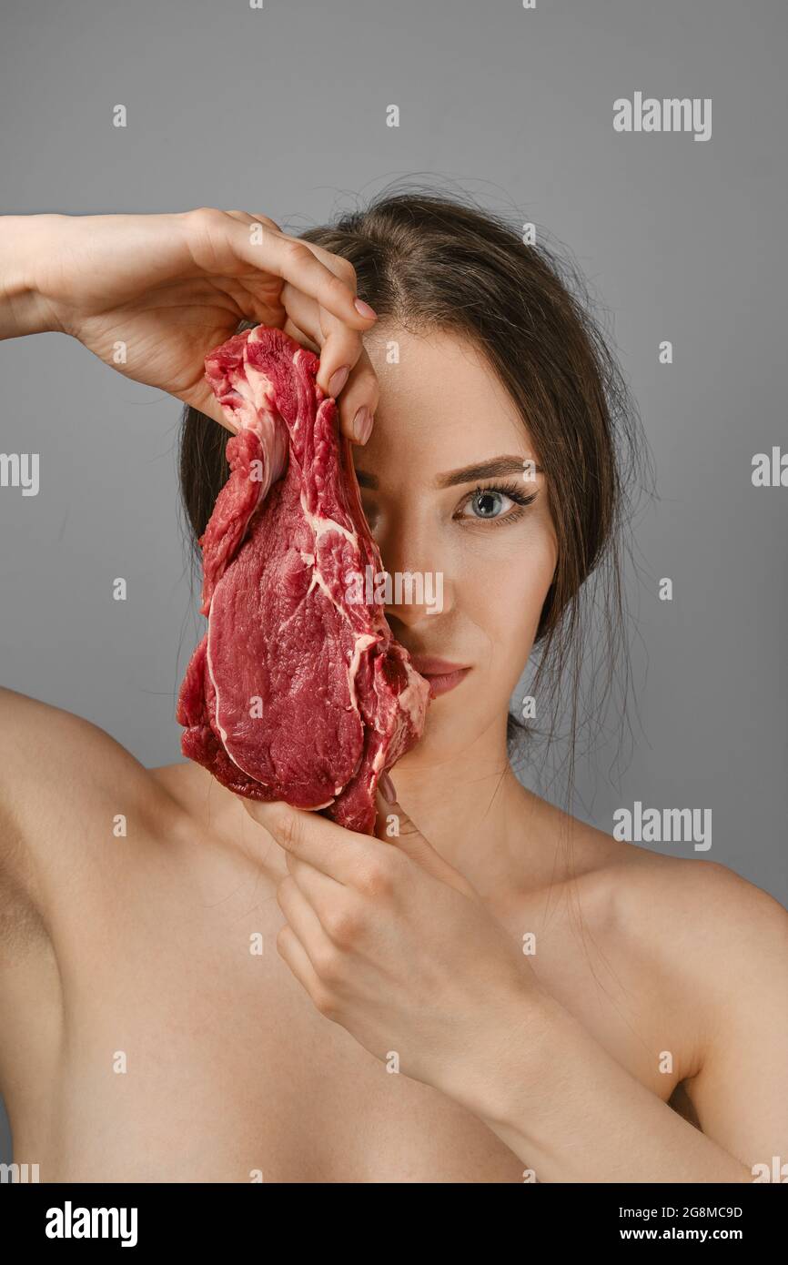 Die junge Frau hält rohes Rindfleisch und bedeckt die Hälfte ihres Gesichts Stockfoto