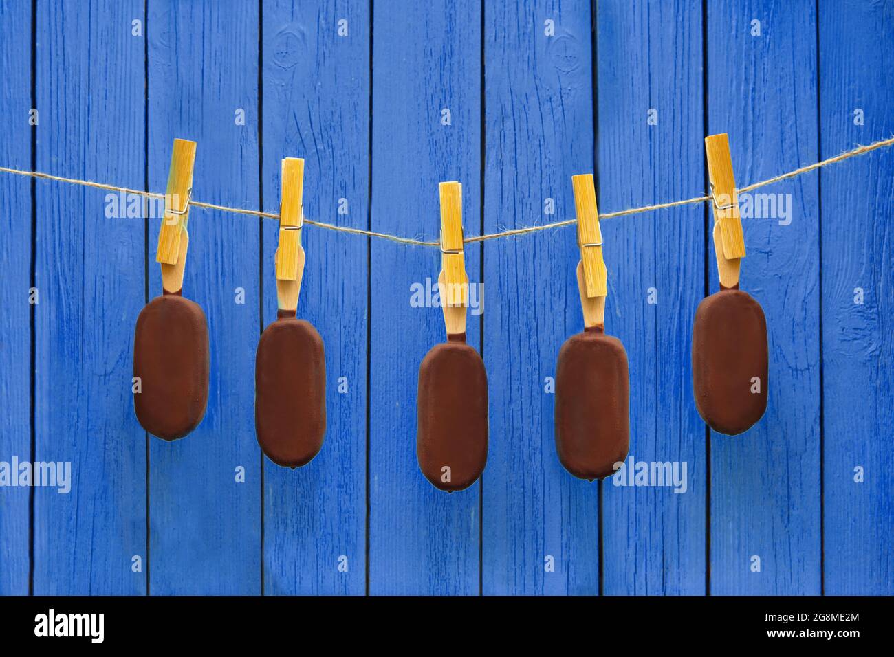 Viele Schokolade Eis hängt am Seil in der Nähe von blauem Hintergrund. Heiße Sommer Dessert und leckeres Essen Konzept Stockfoto