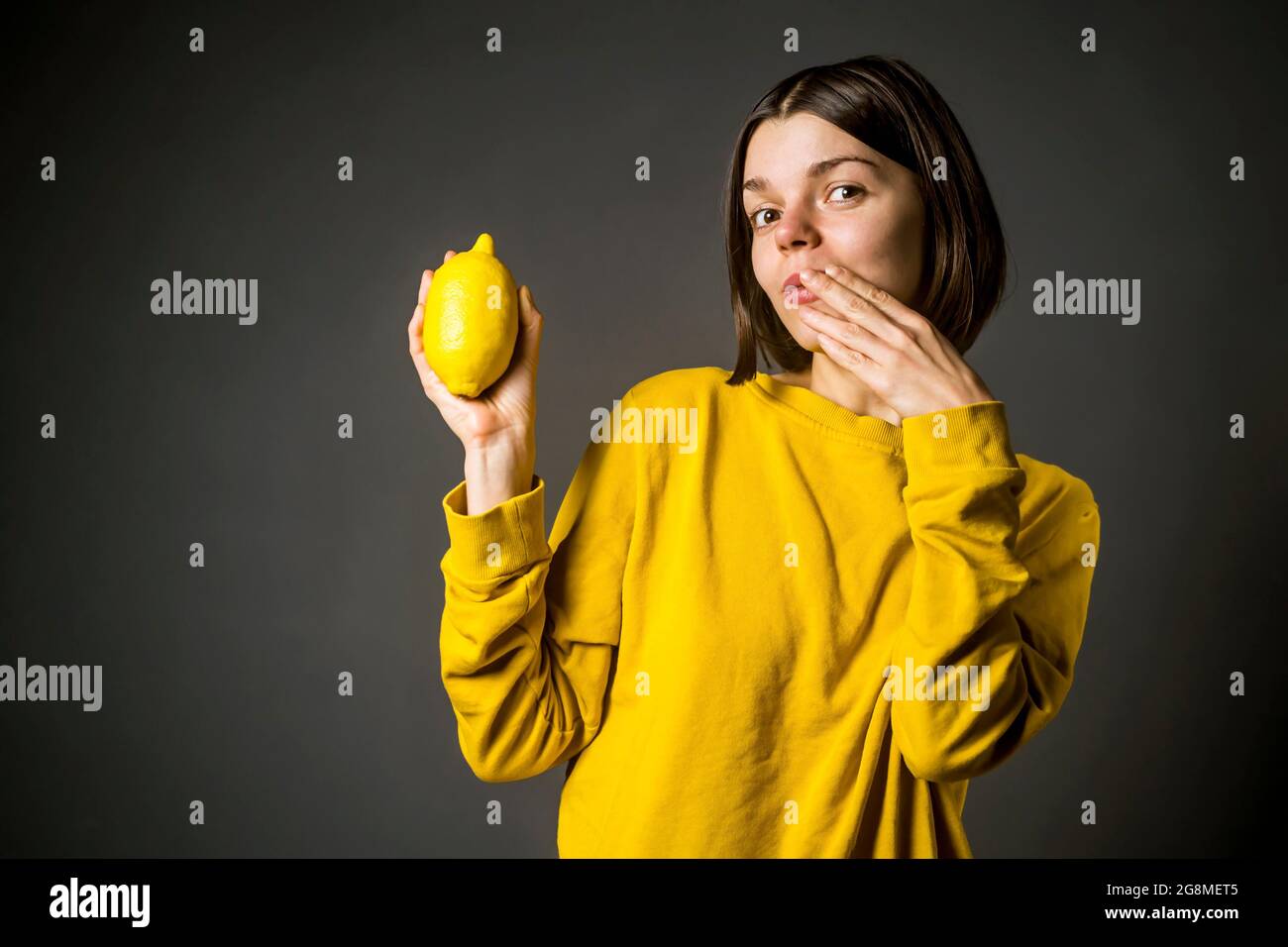 Lustiges Mädchen in einem lässigen gelben Pullover hält eine Zitronenfrucht in der Hand. Stockfoto
