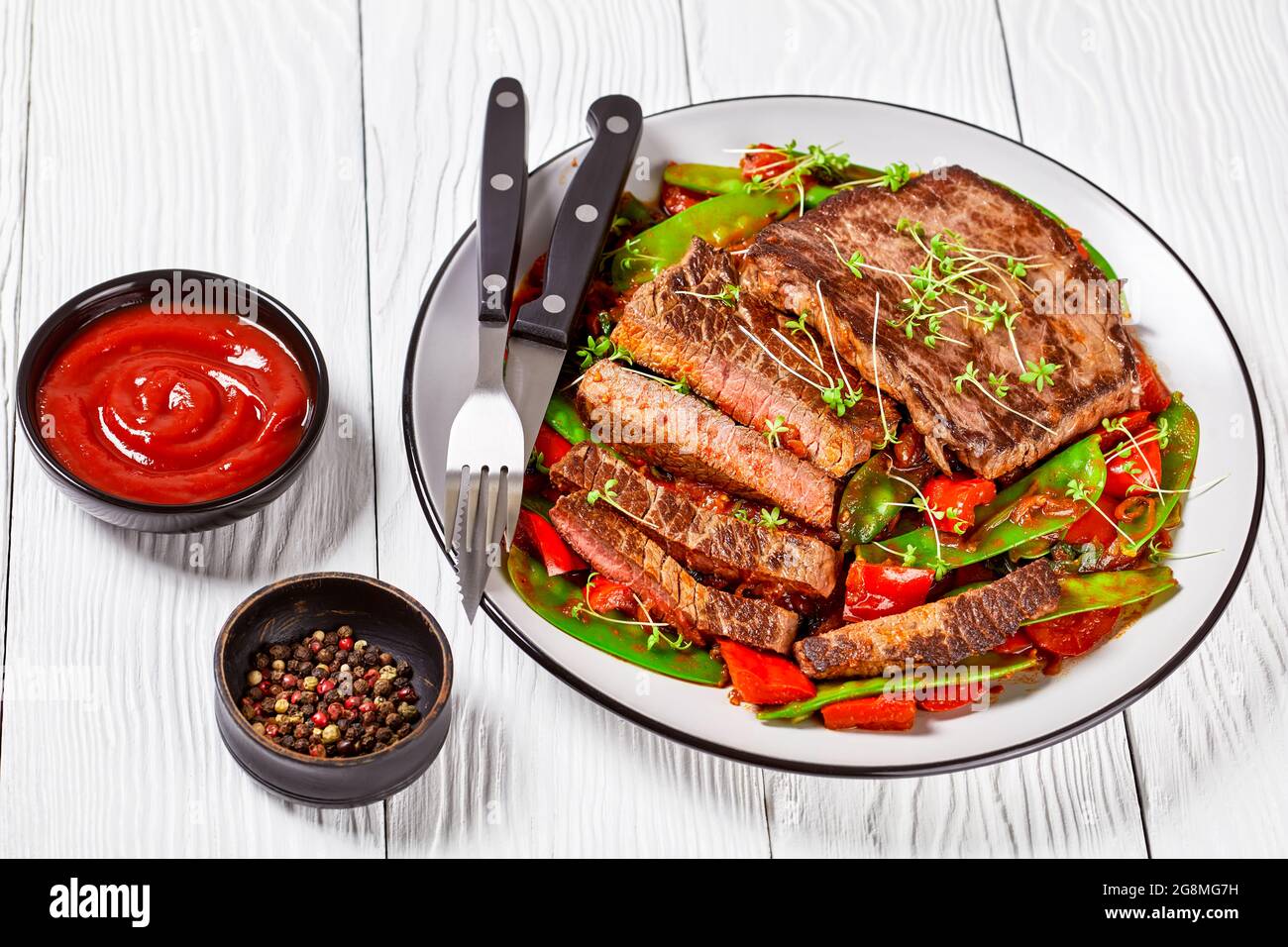 Gegrilltes Rinderhacksteak serviert mit Ragout aus geschmorter Tomatensauce, süßem roten Pfeffer, Schneeerbsenschoten, Zwiebeln und Thymian Stockfoto