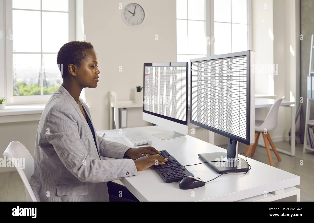 Geschäftsfrau oder Buchhalterin, die am Schreibtisch sitzt und an zwei Desktop-Computern arbeitet Stockfoto