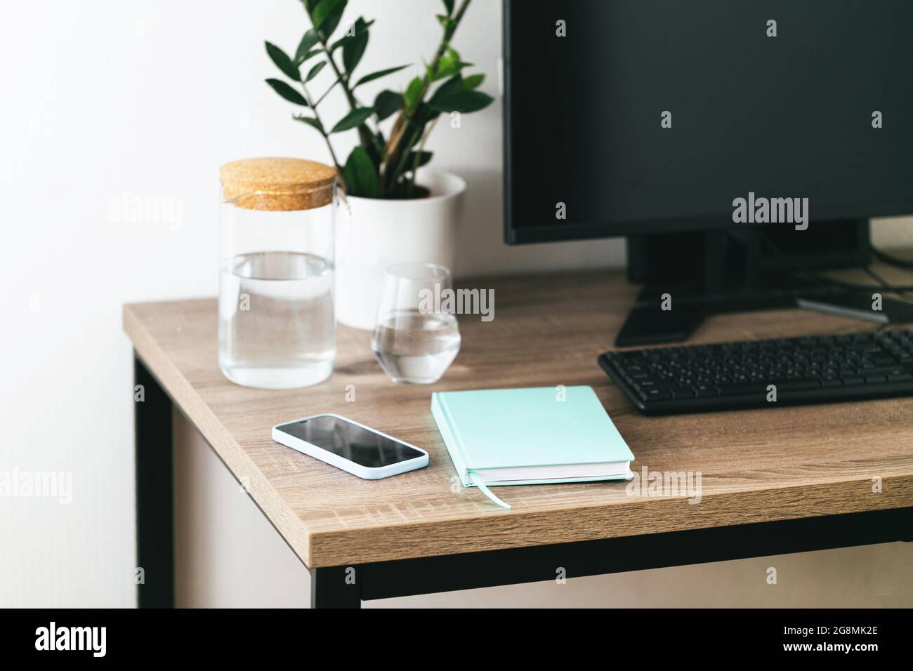 Arbeitsplatz FÜR IT mit Desktop, Tastatur, Telefon, Glas Wasser und einer grünen Pflanze Stockfoto