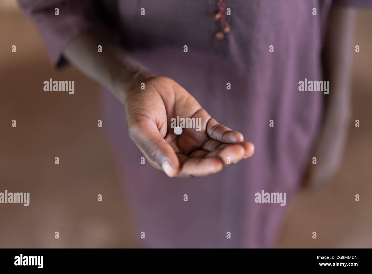 Dies ist ein Bild eines afrikanischen Jungen, der eine medizinische Ergänzung oder Pille in der Hand hält, um die Behandlung eines Mangels oder einer Krankheit zu zeigen. Stockfoto