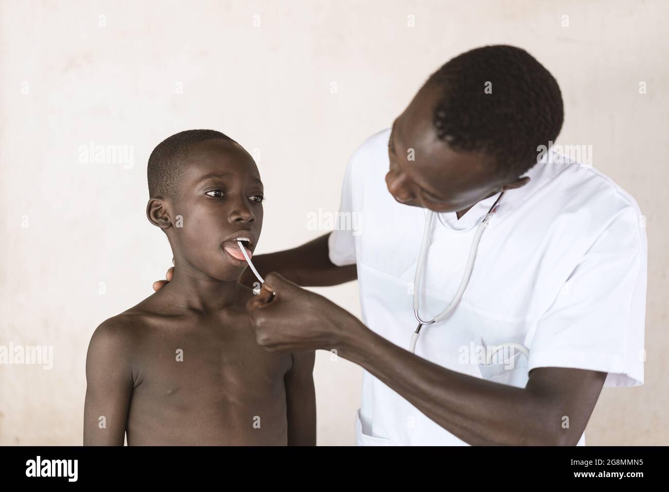 Auf diesem Bild nimmt ein schwarzer Arzt eine Speichelprobe auf einem Tupfer, um die Belastung des Coronavirus bei einem jungen, sehr konformen Jungen zu untersuchen Stockfoto