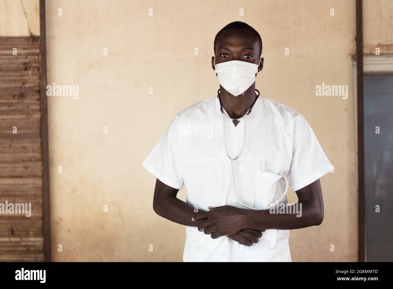 Dieses Bild zeigt einen selbstbewussten jungen afrikanischen Arzt mit einem Stethoskop, das die Hände zusammenfaltet und mit einer Gesichtsmaske und einem Blick direkt in die Kamera zeigt Stockfoto