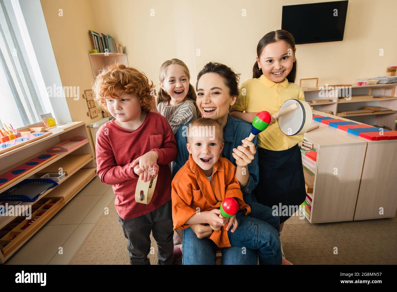 Glücklicher Lehrer mit interrassischen Kindern, die in der montessori-Schule Musikinstrumente spielen Stockfoto