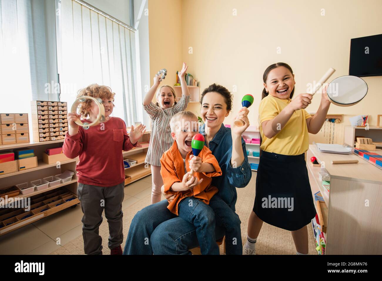 Fröhliche interracial Kinder mit jungen Lehrer spielen Musikinstrumente in montessori Schule Stockfoto
