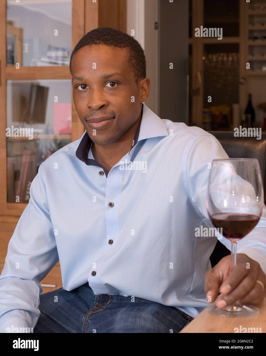 Junger Mann mit blauem Hemd, der sich zu Hause bei einem Glas Rotwein entspannt. Stockfoto