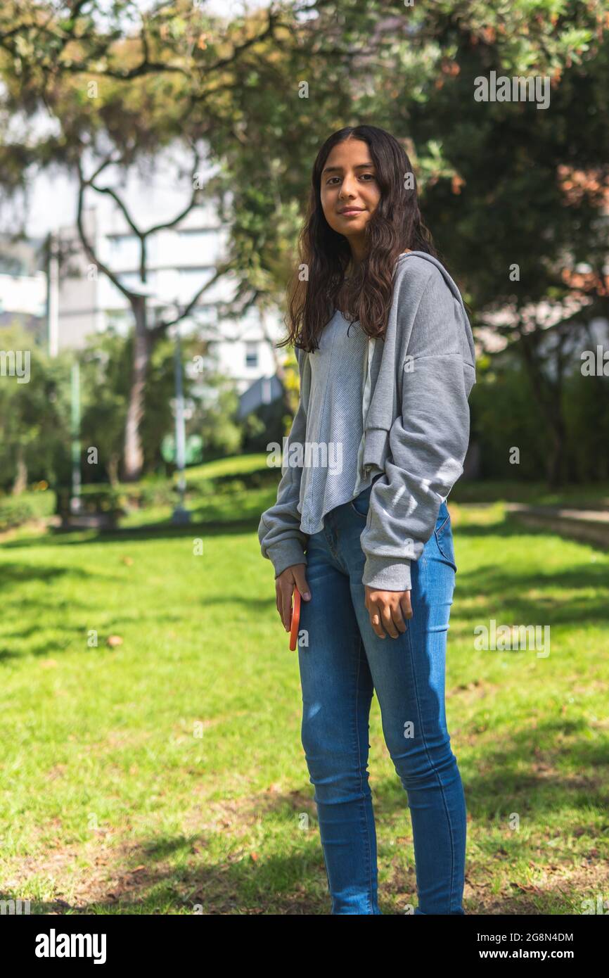 Aufrechtes vertikales Porträt eines brünette Teenagers aus Latina, das morgens in einem Park die Kamera anschaut Stockfoto