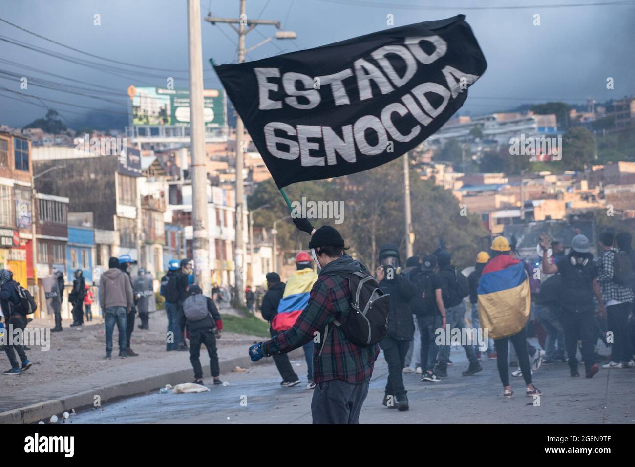 Ein Demonstranten schwenkt eine Flagge mit der Aufschrift „Völkermord-Staat“ während eines neuen Tages von Anti-Regierung-Protesten während der Feier der Unabhängigkeit Kolumbiens von spanien im Jahr 211, Proteste, die nach einer Intervention der kolumbianischen Bereitschaftspolizei ESMAD am 20. Juli 2021 in Bogota, Kolumbien, zu Zusammenstößen in verschiedenen Städten geführt wurden. Stockfoto