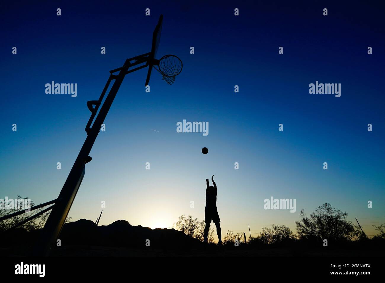 Eine Silhouette eines Basketballspielers, der seinen Schuss bei Sonnenuntergang in der Wüste übt. Stockfoto