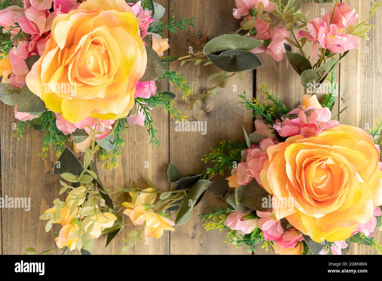 Hintergrund mit künstlichen Blumen auf einem Holztisch. Gelbe Rosen und rosa Blüten. Weicher Fokus Stockfoto