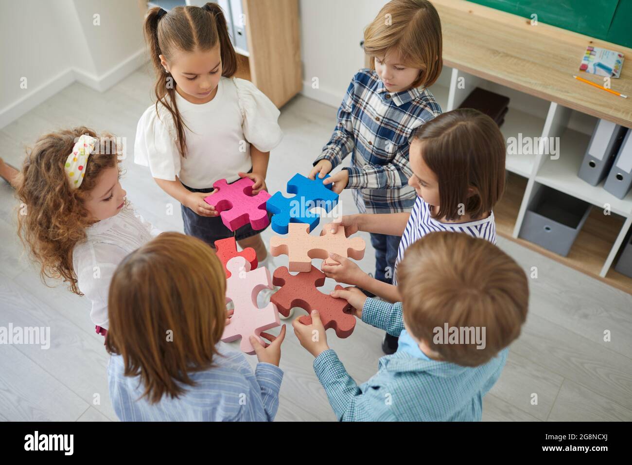 Team von Schulkindern stehen im Klassenzimmer und fügen Teile des Puzzles Stockfoto