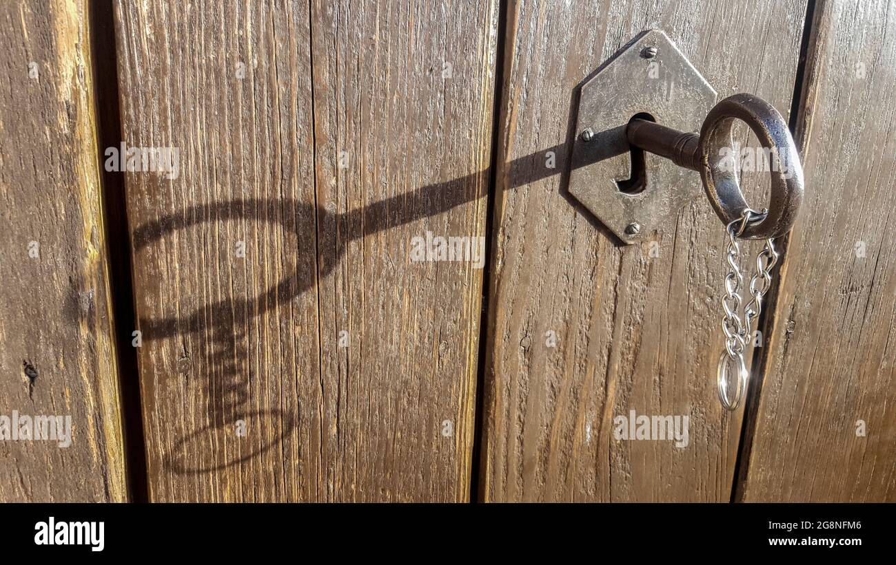 Rural Schlüsselschloss mit hängender Kette. Der Schlüssel wirft einen Schatten über die verwitterte Holzstruktur Stockfoto