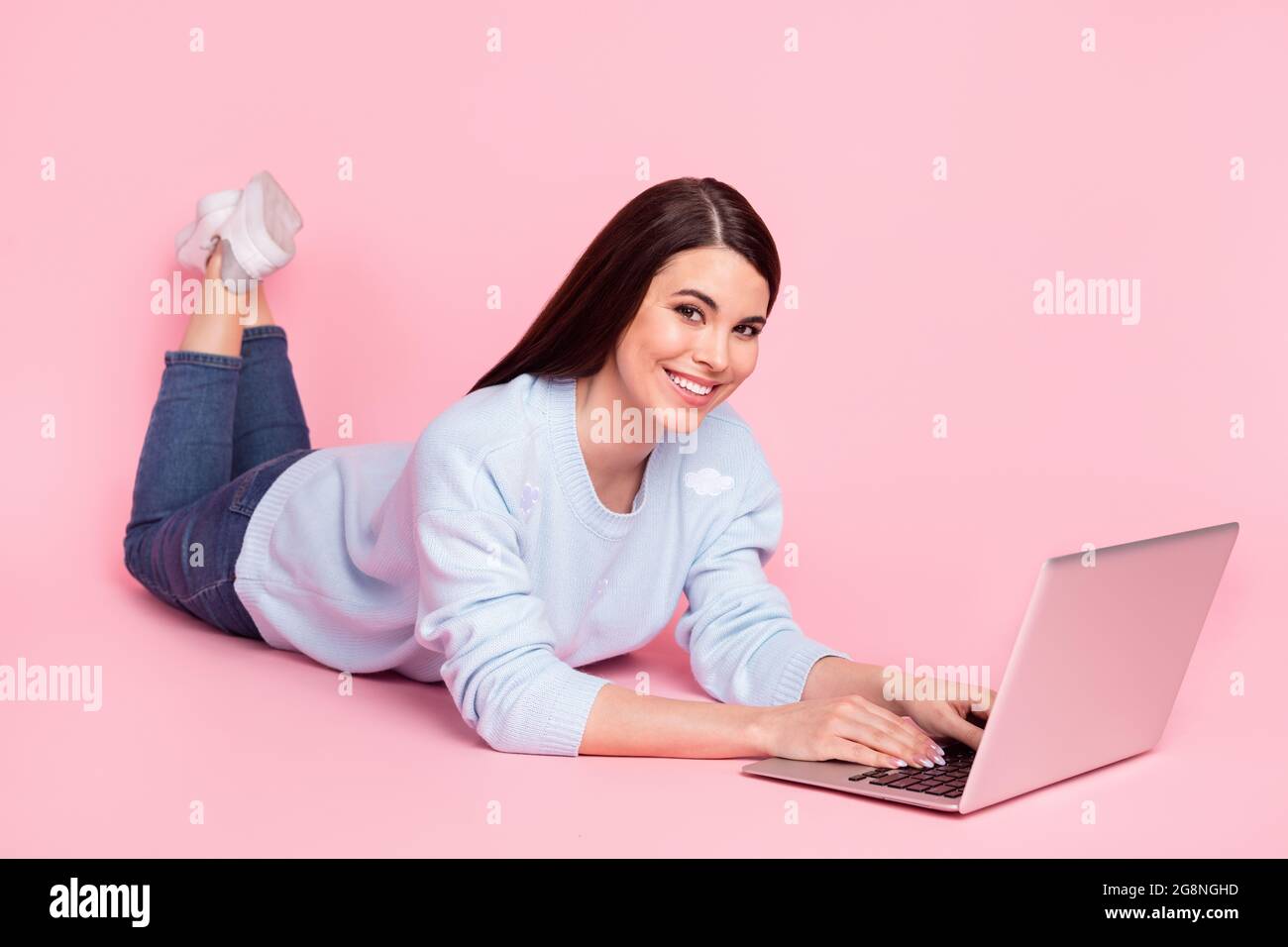 In voller Größe Foto von schönen optimistisch Brünette Frisur Dame Lüge Arbeit Laptop tragen Hemd Jeans auf rosa Hintergrund isoliert Stockfoto