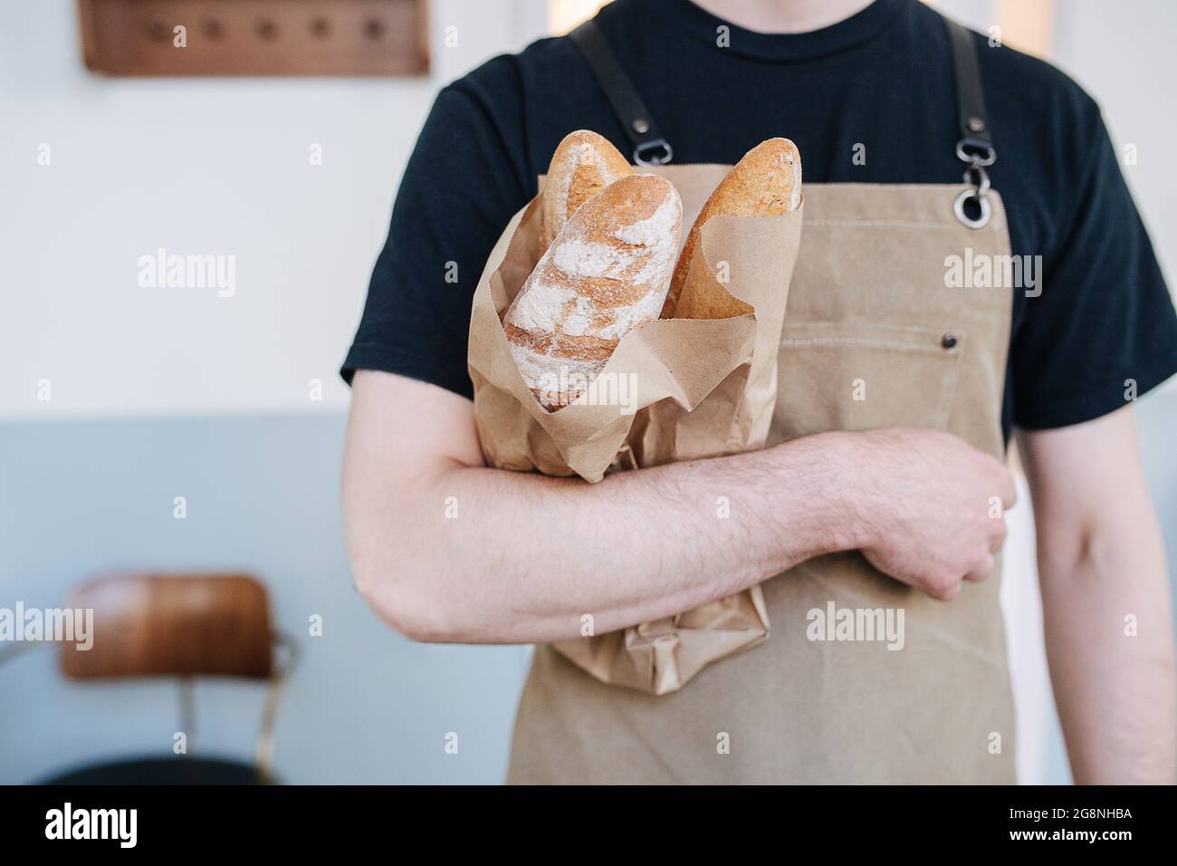 Papiertüte mit frischen Baguettes, die von einem männlichen Bäcker in beigefarbener Schürze gehalten werden Stockfoto