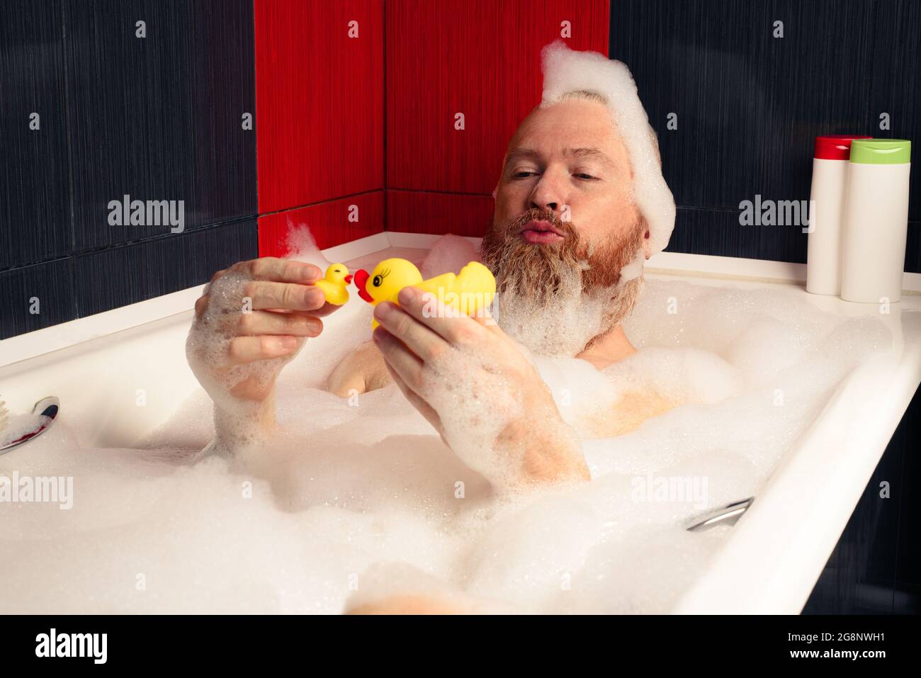 Netter lustiger bärtiger Mann, der mit Gummienten im Schaumbad spielt und sich zu Hause entspannt. Stockfoto