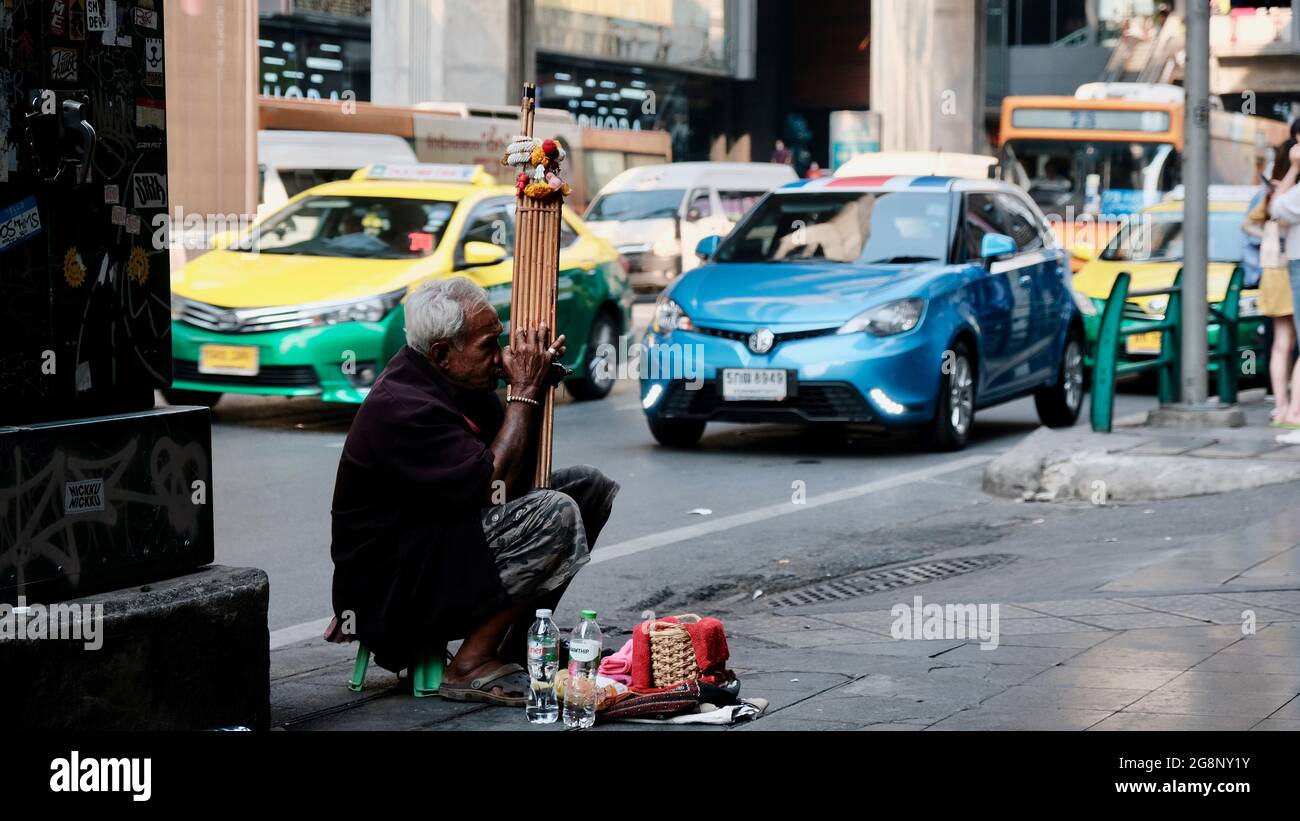 Der traditionelle thailändische Old man Street Musiker Siam Square Wirtschaft und Wirtschaft Bangkok Thailand spielt auf einem Hocker um Veränderung Stockfoto