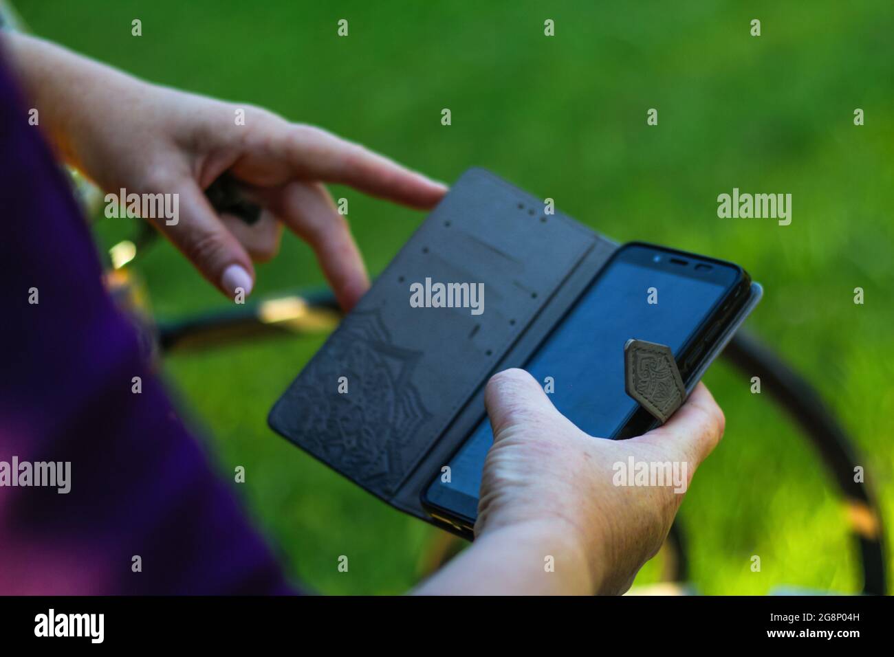 Unschärfe-Unschärfe-Nahaufnahme weibliche Hände suchen auf dem Telefon außerhalb, im Freien. Erwachsene Frau in lila Bluse mit Smartphone, während sie auf einer Bank in der p sitzen Stockfoto