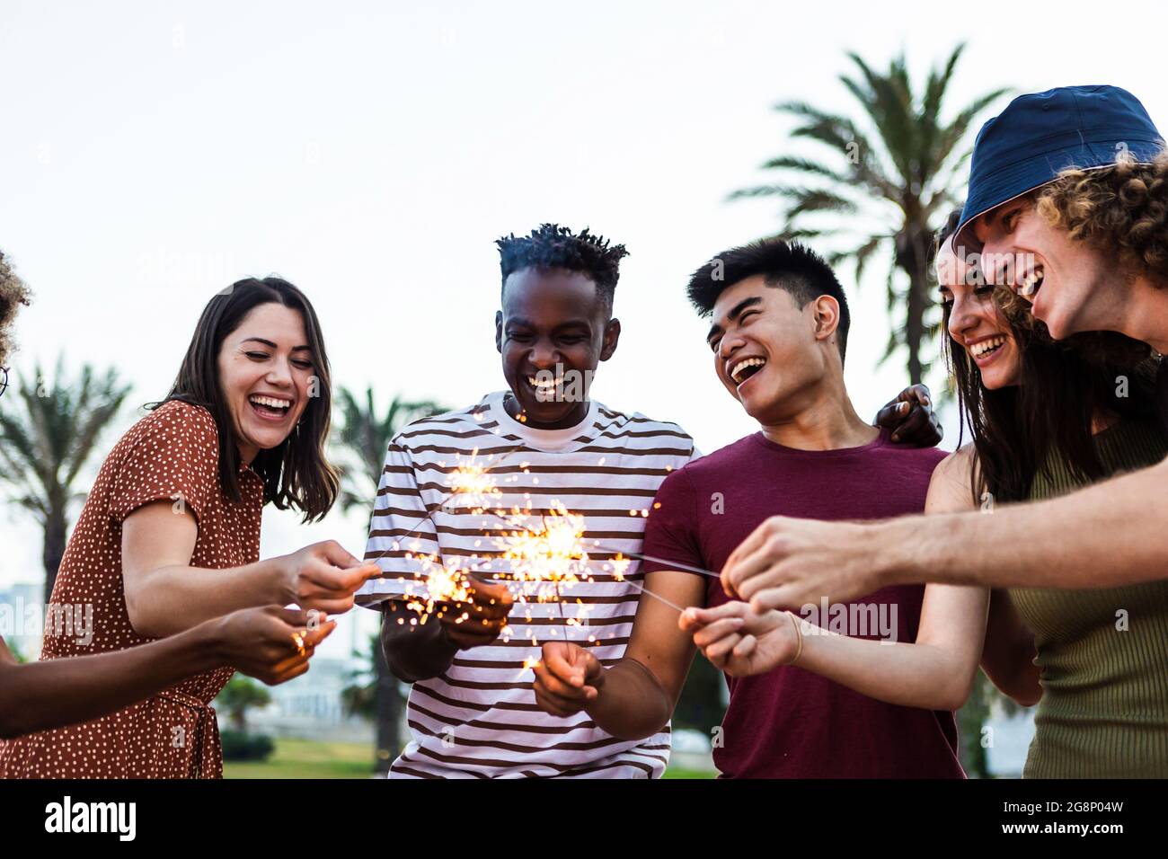 Fröhliche, multirassische Menschen, die Sommerparty am Strand genießen - eine vielfältige Gruppe junger Erwachsener, die gemeinsam mit Wunderkerzen im Freien feiern - Stockfoto