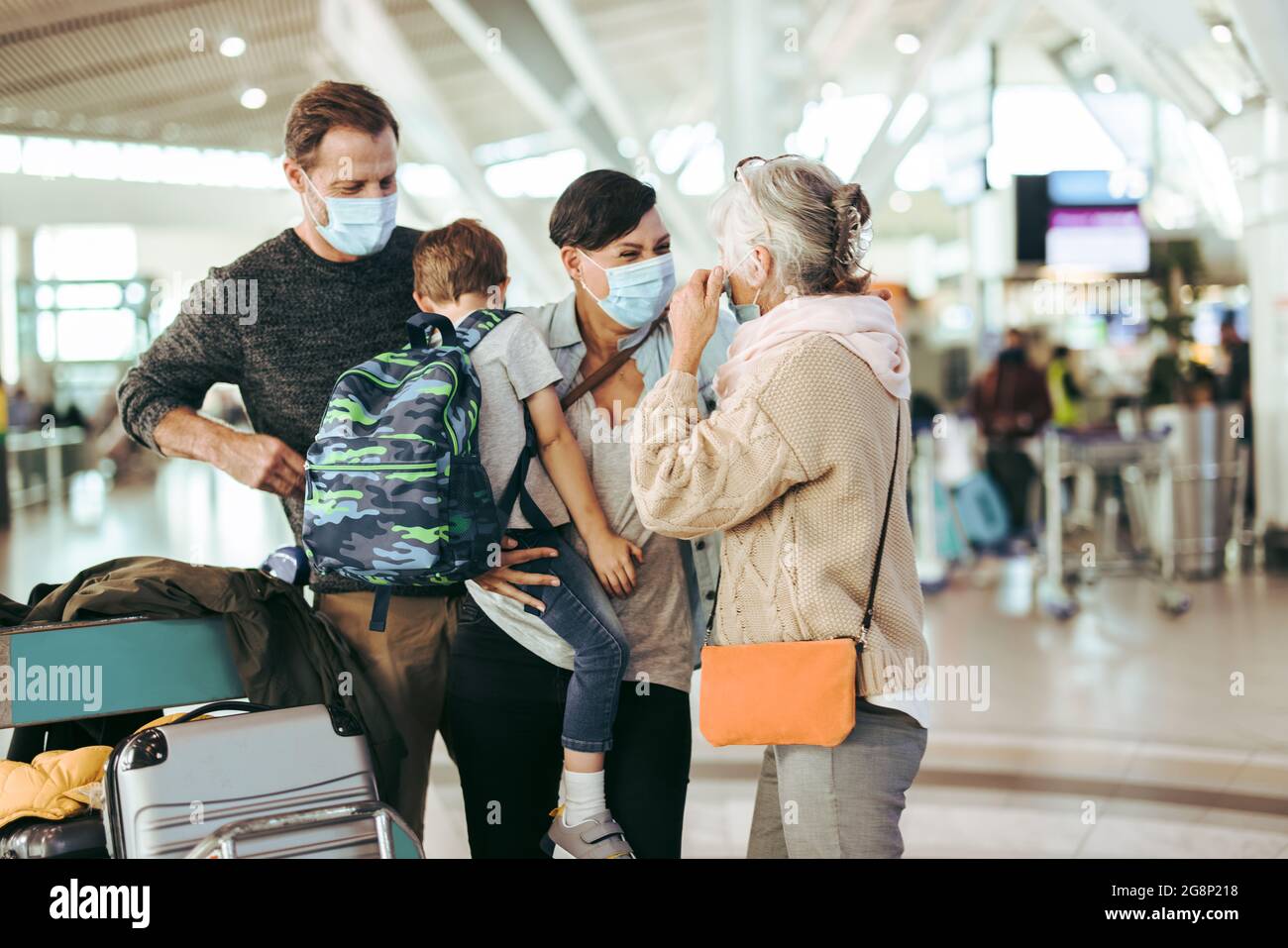 Eine ältere Frau trifft ihre Familie, die nach der Sperrung der Pandemie am Flughafen ankommt. Dreiköpfige Familie mit Gesichtsmaske trifft Großmutter am Flughafen. Stockfoto