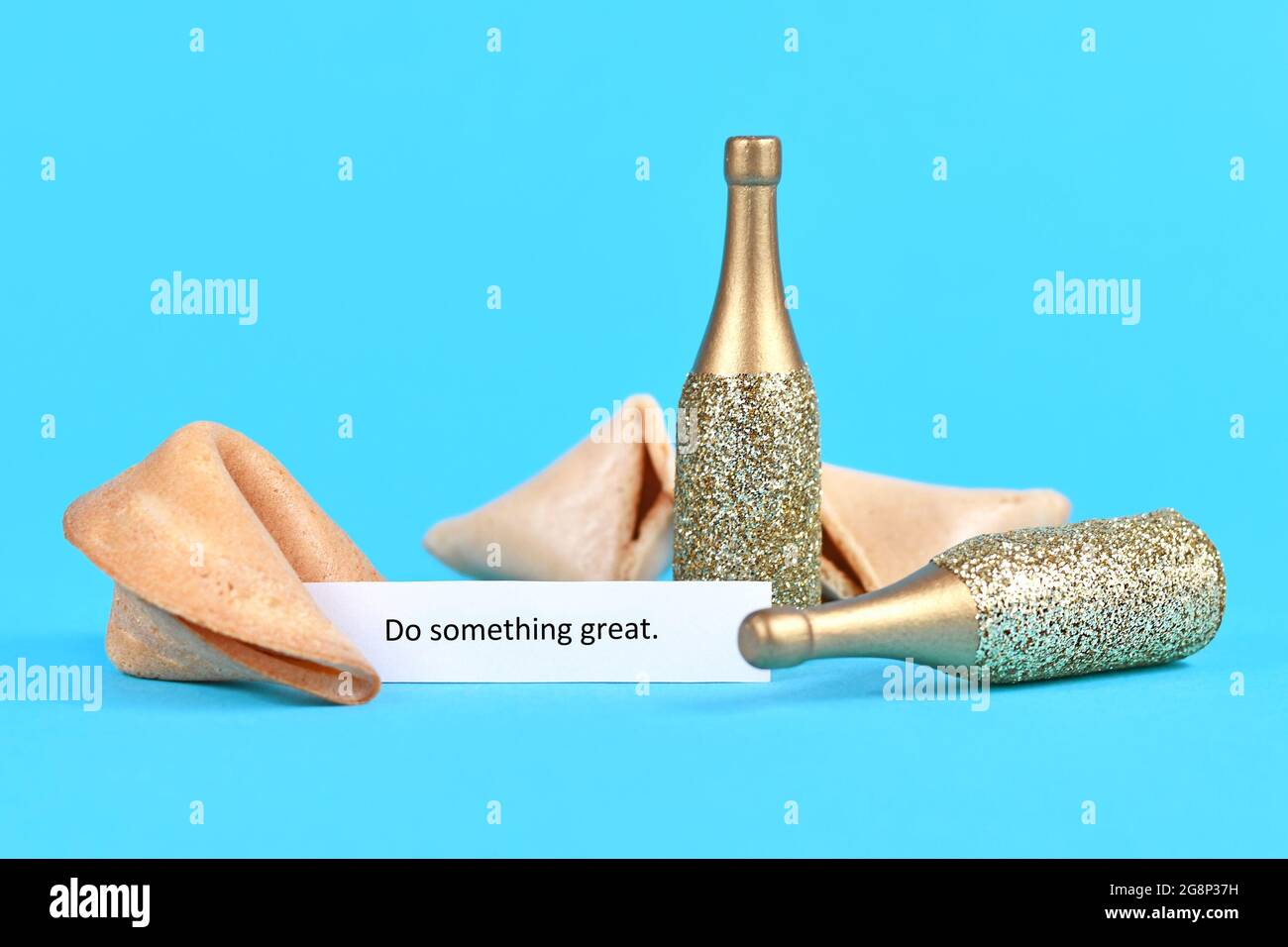 Öffnen Sie den Fortune Cookie mit einem motivierenden Text, in dem es heißt: „Do something great“ mit goldenen Champagnerflaschen Stockfoto