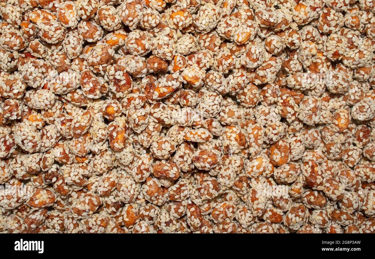 Hintergrund aus Erdnüssen oder Rosinen mit braunem Karamell und Sesam bedeckt. Karamellisierte Nüsse Hintergrund Stockfoto