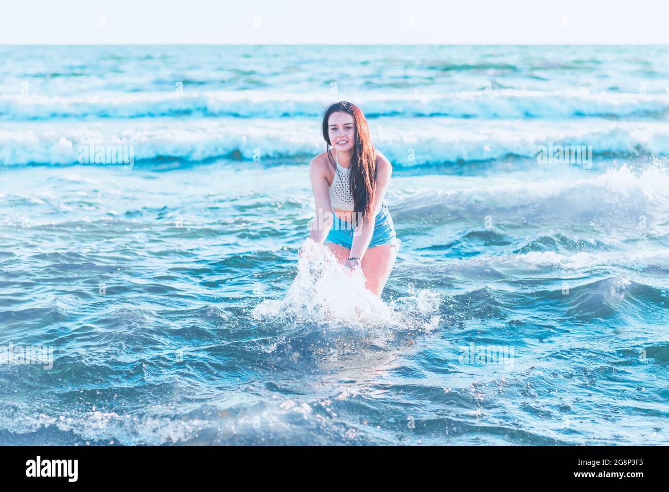 Junge Frau, die im Sommer im Meer spielt. Frau macht im Meerwasser planschen. Fröhliche junge Frau, die Spaß am Strand hat. Sie spritzt im Meereswat Stockfoto