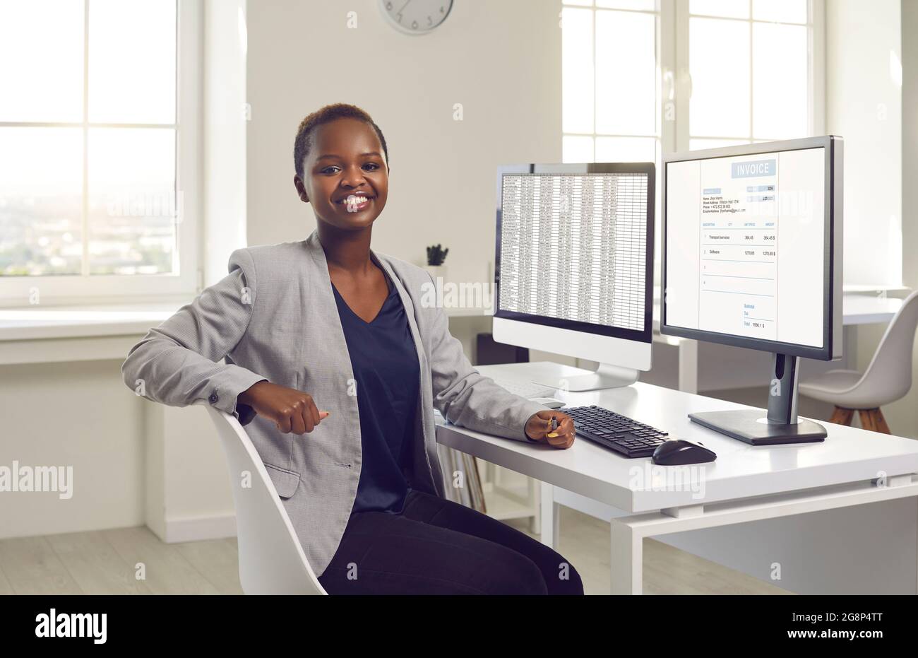 Glückliche schwarze Geschäftsfrau oder Buchhalterin, die am Schreibtisch mit Desktop-Computern sitzt Stockfoto