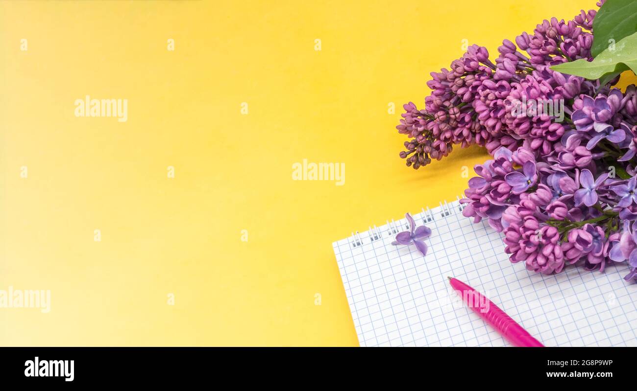 Notizblock mit Stift und Blumen. Spiralnotizbuch und Stift. Notebook-Flieder auf gelbem Hintergrund. Stockfoto