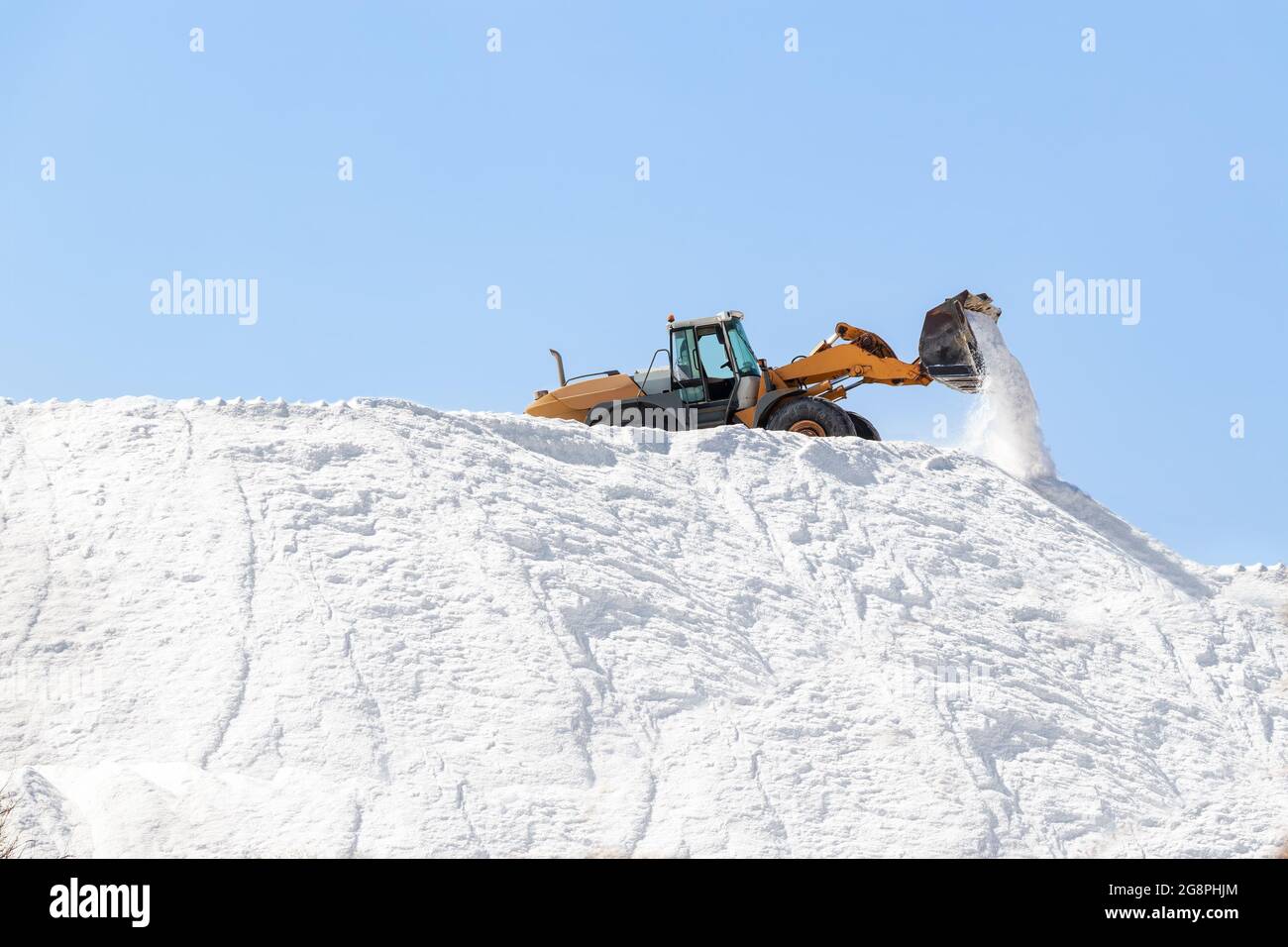 Bagger arbeiten in einem riesigen Salzstapel in Salzwerken. Meersalz, das durch die Verdunstung von Meerwasser entsteht. Stockfoto