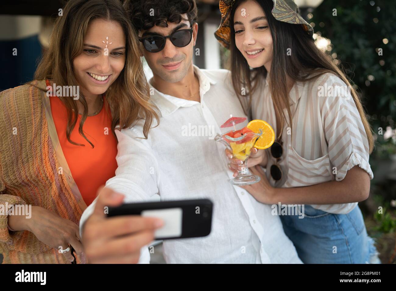 Eine Gruppe lächelnder junger Menschen, die ihr Handy beobachten und gemeinsam Spaß haben. Freunde, die Tech-Konzept verwenden. Stockfoto