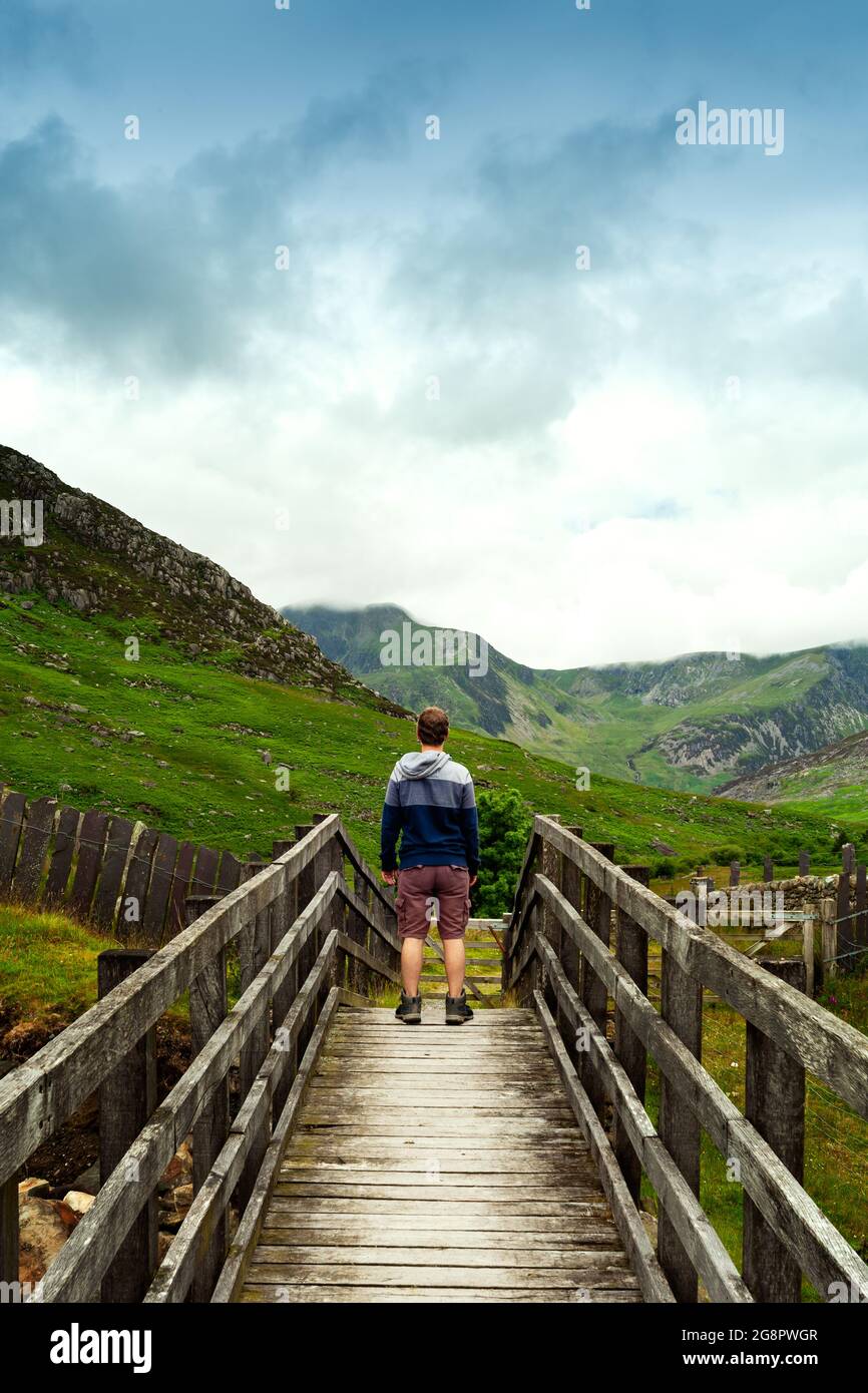 Mann, der über eine Brücke über die Berge von Tryfan und Pen yr Ole Wen blickt Stockfoto