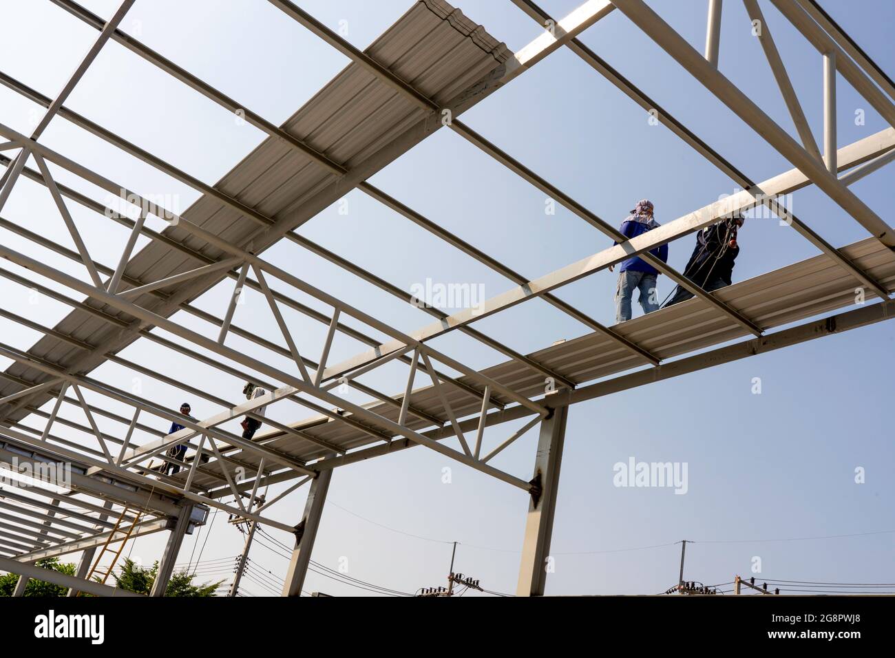 Drei Männer installieren das Dachblech an der leichten Truss- und Rahmenkonstruktion aus Stahl. Stockfoto