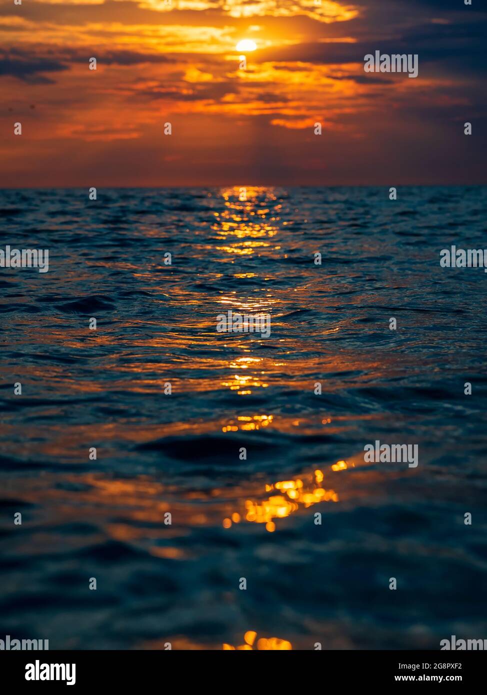 Sonnenuntergang mit Wolken, warmen Farben und Wellen im Ozean. Stockfoto