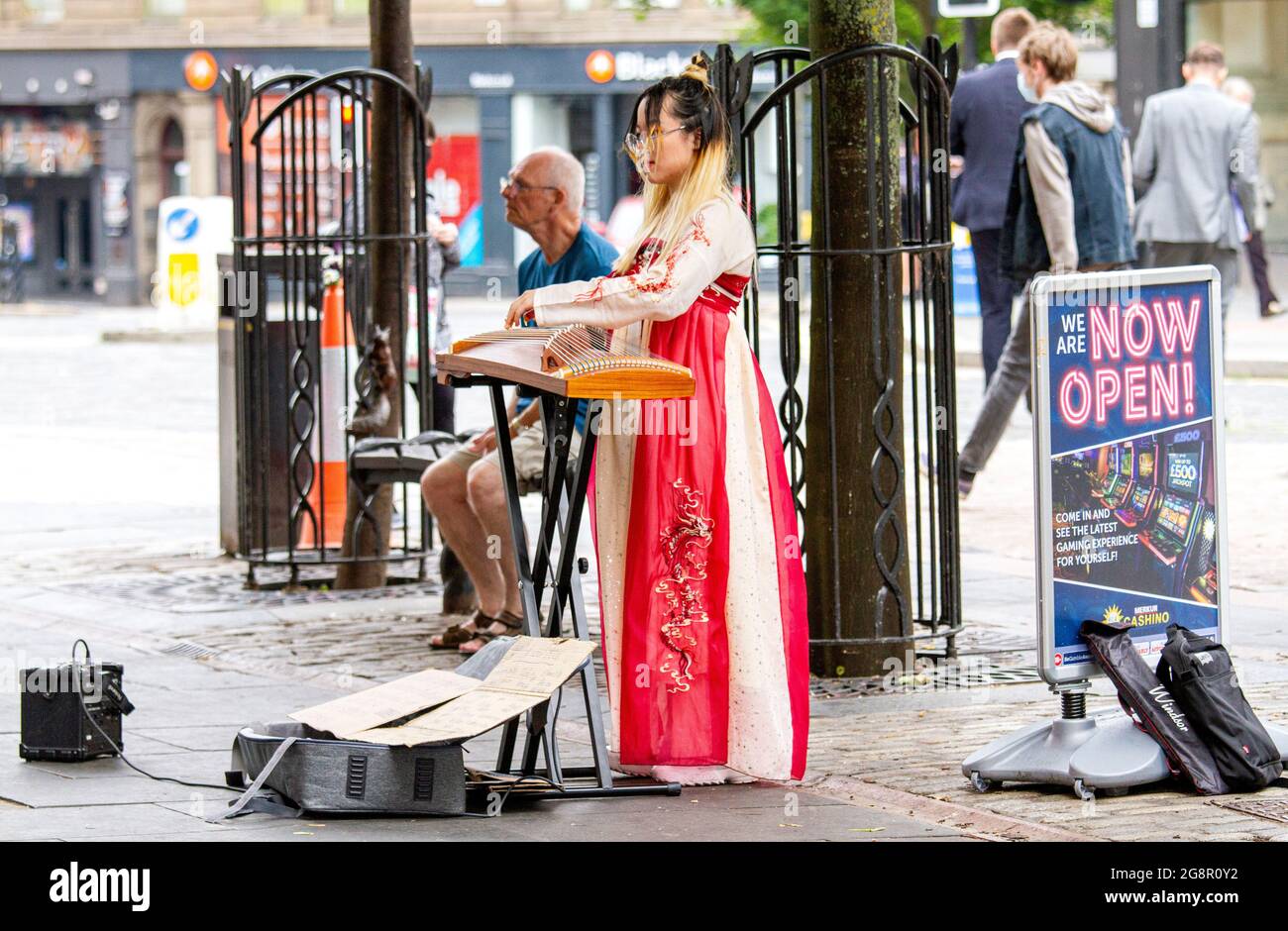 Dundee, Tayside, Schottland, Großbritannien. Juli 2021. UK Wetter: Ein heller, feuchter Tag in Nordostschottland mit Temperaturen von bis zu 21 Grad Eine junge südostasiatische Frau in traditionellem Kleid nimmt den Tag mit, indem sie klassische chinesische Musik mit ihrer Zither spielt, einer Figur, die ein Saiteninstrument im Stadtzentrum von Dundee zupft. Kredit: Dundee Photographics/Alamy Live Nachrichten Stockfoto