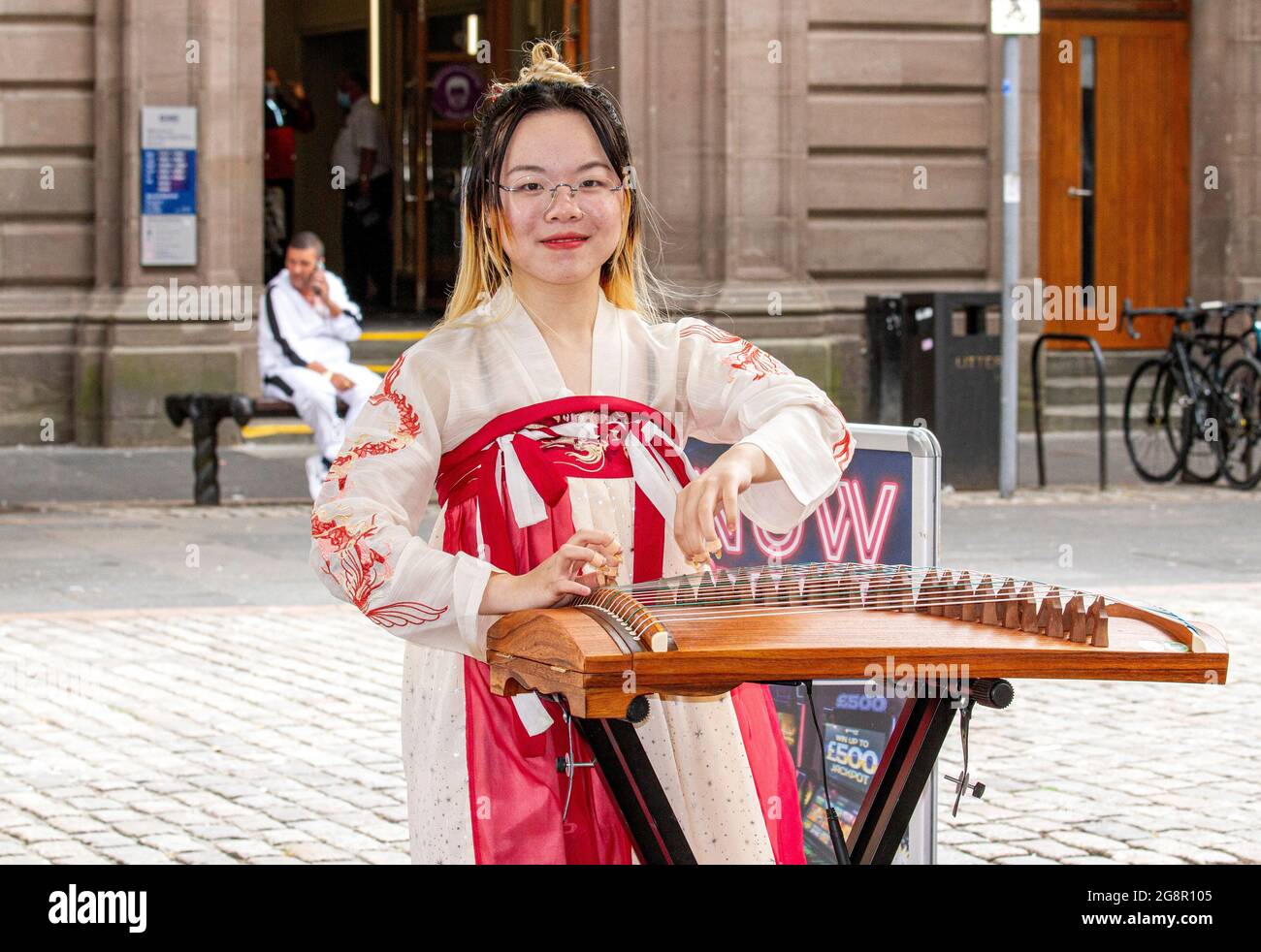 Dundee, Tayside, Schottland, Großbritannien. Juli 2021. UK Wetter: Ein heller, feuchter Tag in Nordostschottland mit Temperaturen von bis zu 21 Grad Eine junge südostasiatische Frau in traditionellem Kleid nimmt den Tag mit, indem sie klassische chinesische Musik mit ihrer Zither spielt, einer Figur, die ein Saiteninstrument im Stadtzentrum von Dundee zupft. Kredit: Dundee Photographics/Alamy Live Nachrichten Stockfoto