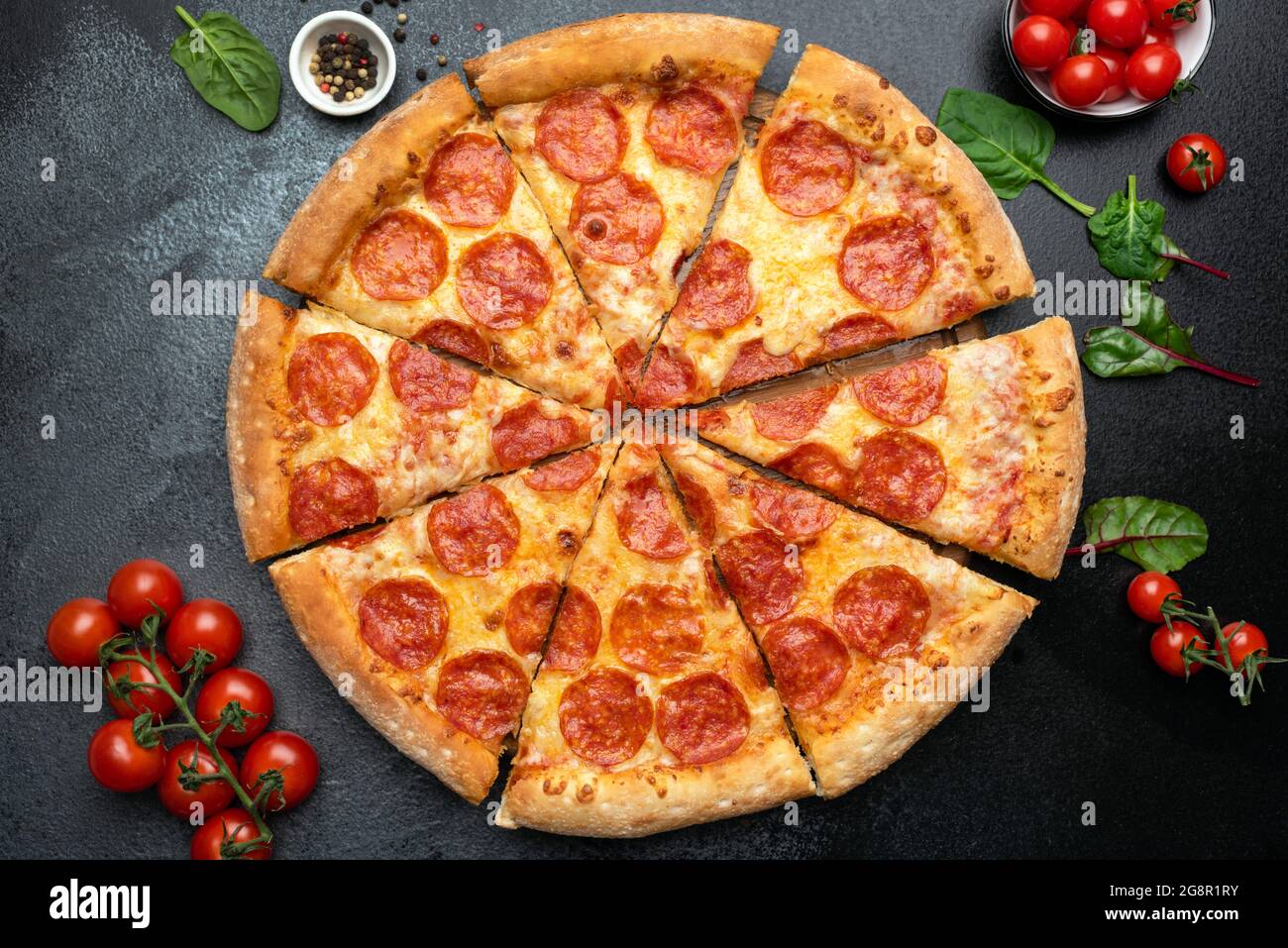 Pepperoni Pizza auf schwarzem Beton-Hintergrund geschnitten, Draufsicht. Scharfe Pizza in Pizzascheiben geschnitten Stockfoto