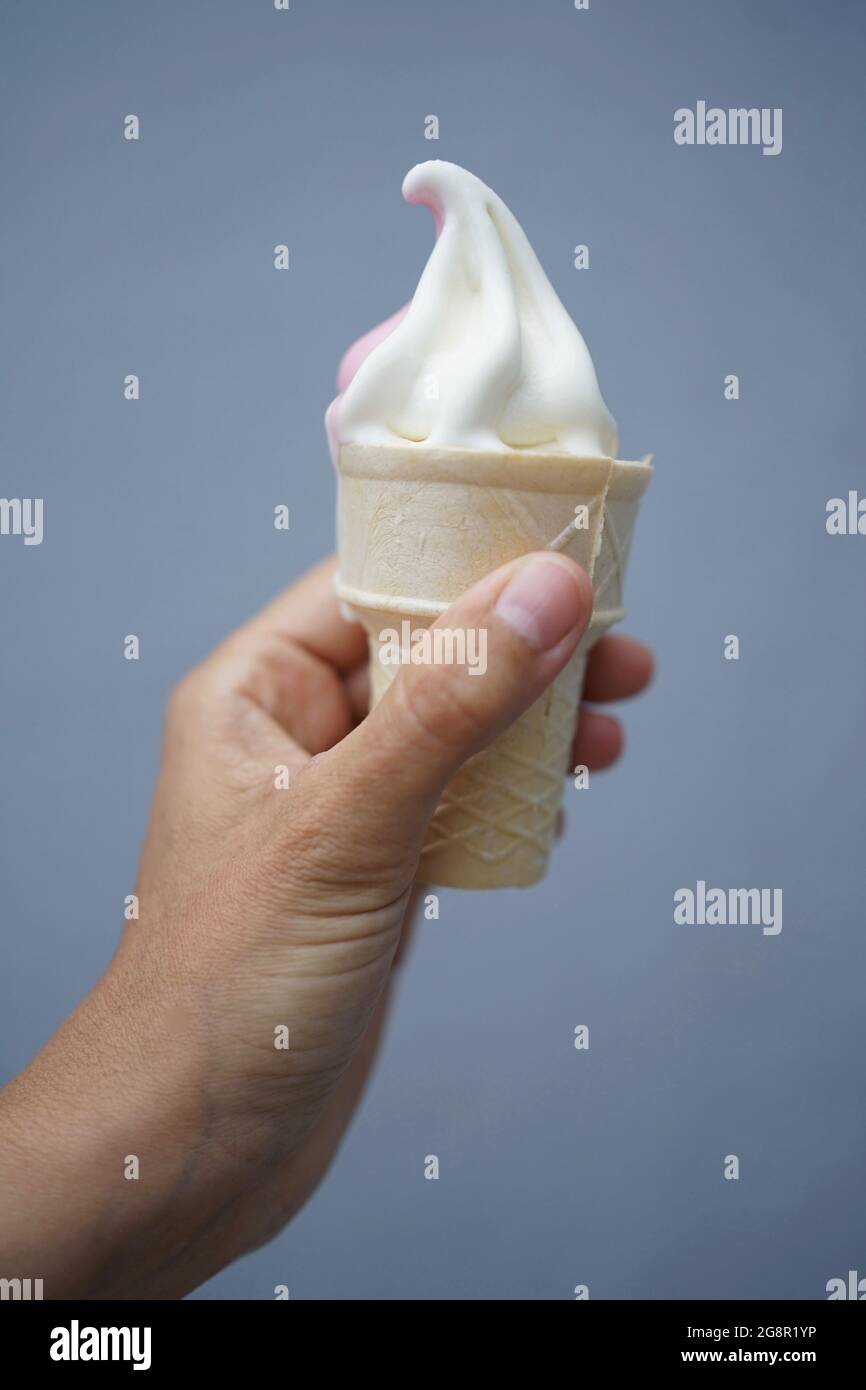 Hand hält Softeis in Waffel mit grauem Hintergrund Stockfoto