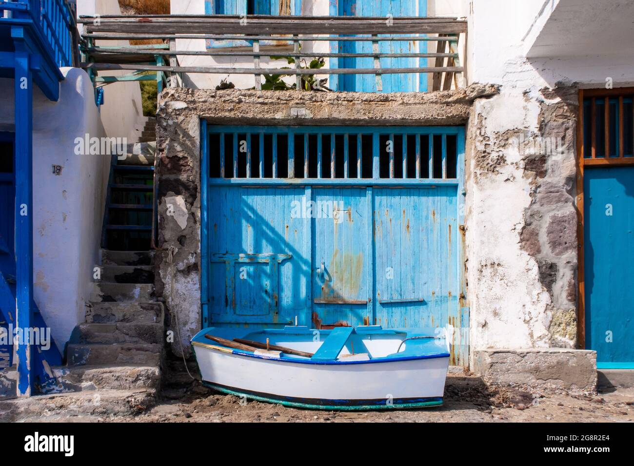 Leuchtend blaue Garagentore mit einem kleinen Holzboot vor dem Fischerdorf Greek Klima - dem buntesten Dorf Griechenlands. Stockfoto