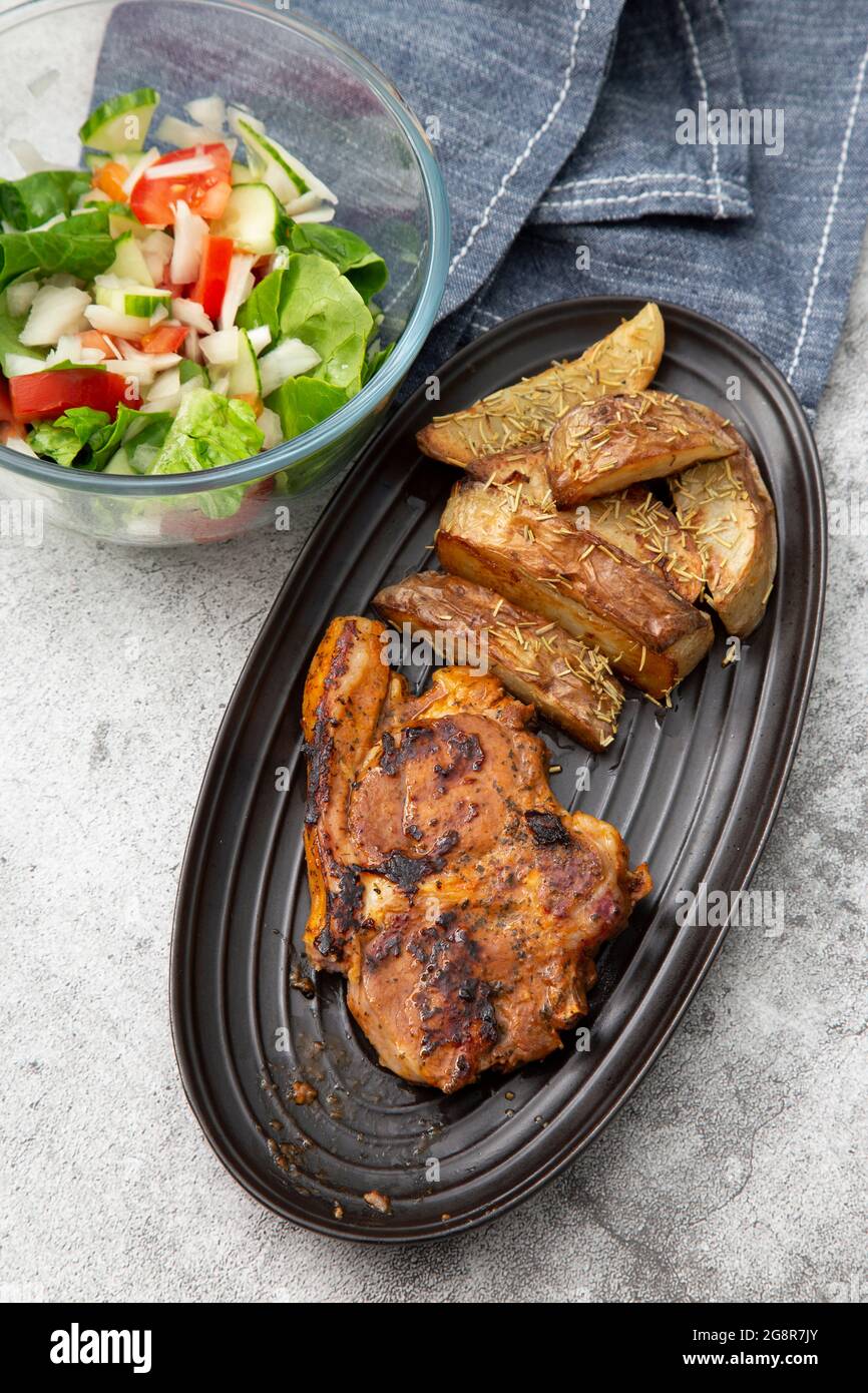 Lammkotelett auf einem schwarzen Gericht mit mit Rosmarin überzogenen Kartoffelkeilen und Salat Stockfoto