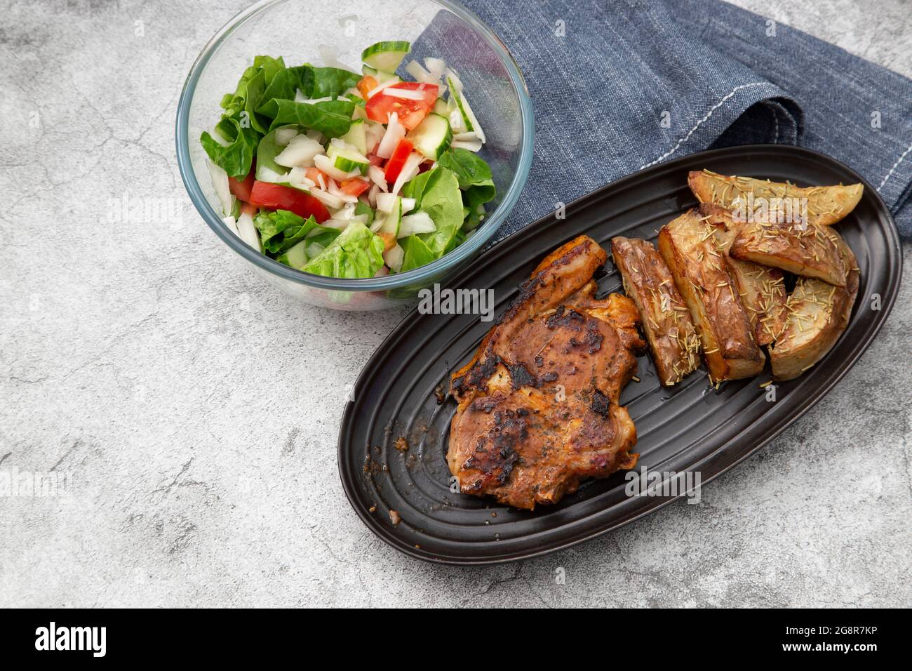 Lammkotelett auf einem schwarzen Gericht mit mit Rosmarin überzogenen Kartoffelkeilen und Salat Stockfoto