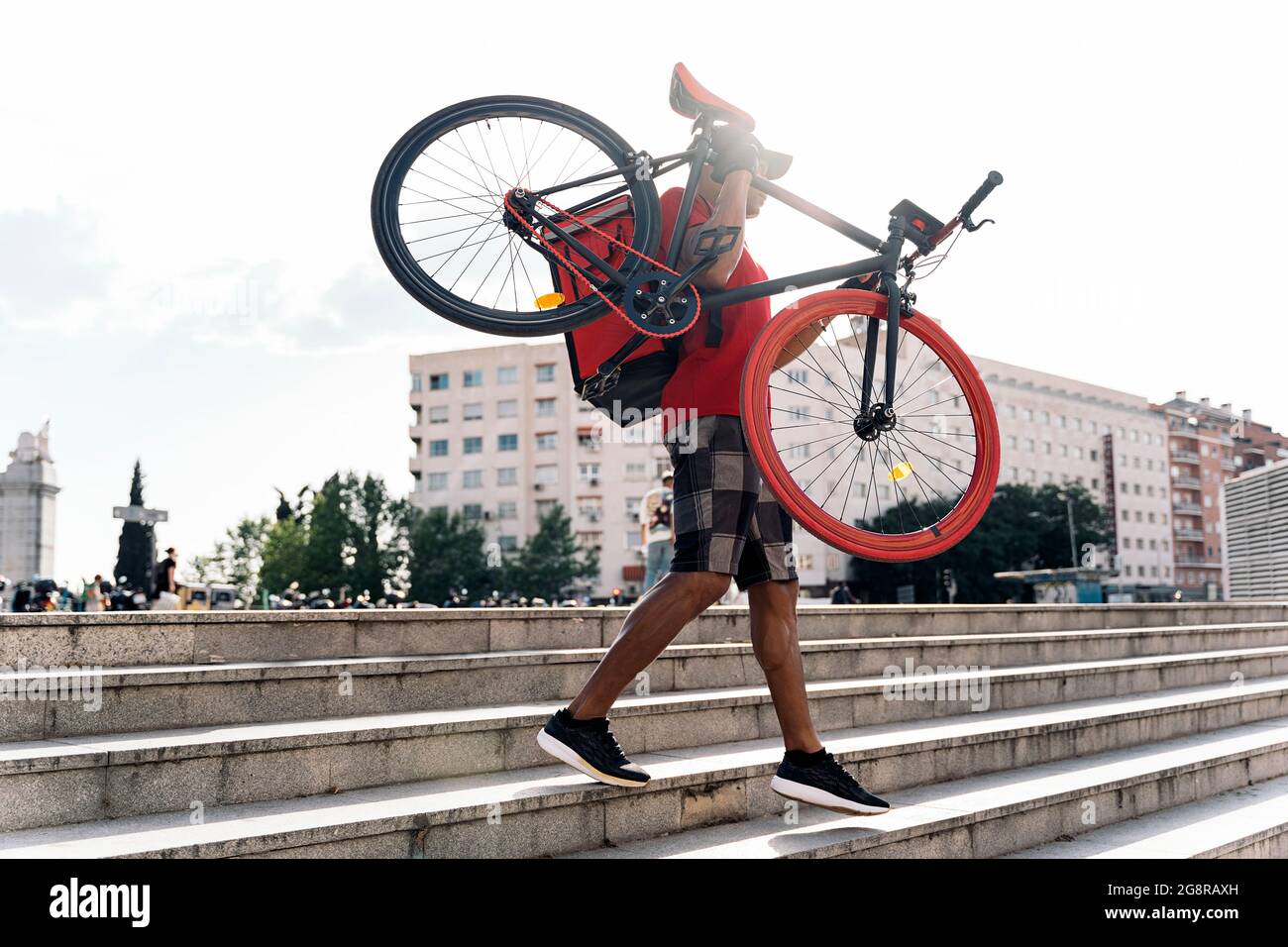 Nicht anerkannter Bote, der eine Mütze trägt und sein Fahrrad in der Stadt trägt, um ein Paket zu liefern. Stockfoto